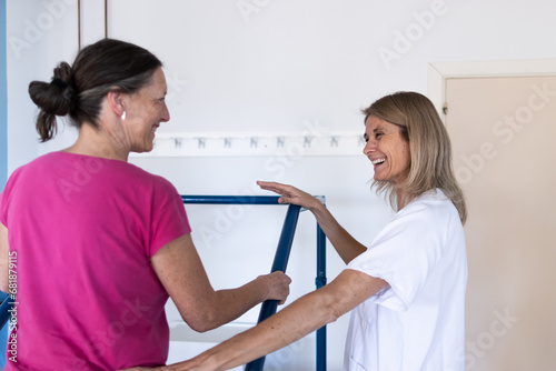 A nurse stands in the hospital next to her patient as they look at each other and laugh together.