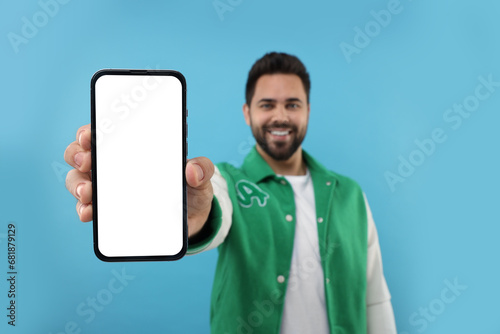 Young man showing smartphone in hand on light blue background, selective focus. Mockup for design