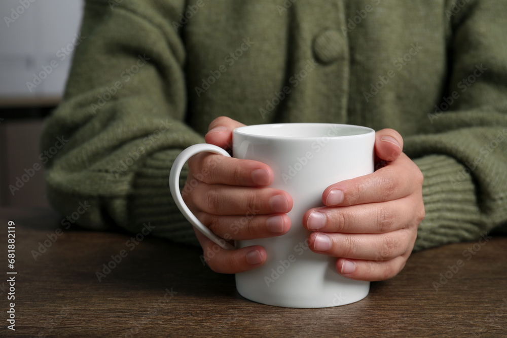 Woman holding white mug at wooden table, closeup Woman holding white mug at wooden table, closeup