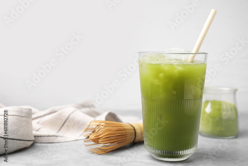 Glass of delicious iced green matcha tea and bamboo whisk on light grey table, space for text