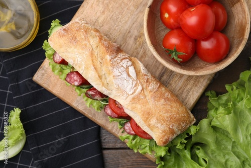 Delicious sandwich with sausages and vegetables on wooden table, flat lay