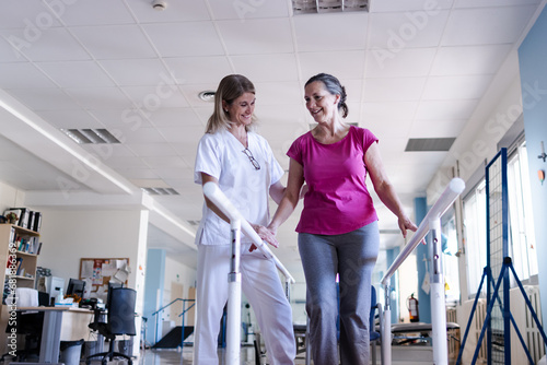 The physiotherapist and her patient are doing rehabilitation on the parallel bars in the gym. They are with surprised faces.