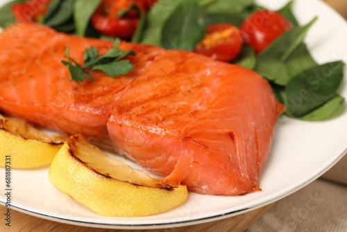 Tasty grilled salmon with basil, tomatoes and lemon on table, closeup