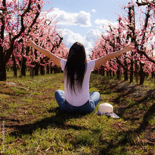 Unrecognizable woman sitting on her back with open arms in a field of peach trees with flowers in Aitona, Catalonia, Spain. photo