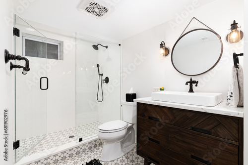 A cozy bathroom with a dark wood cabinet and vessel sink, an mosaic pattern tile flooring, and herringbone shower tile walls. 