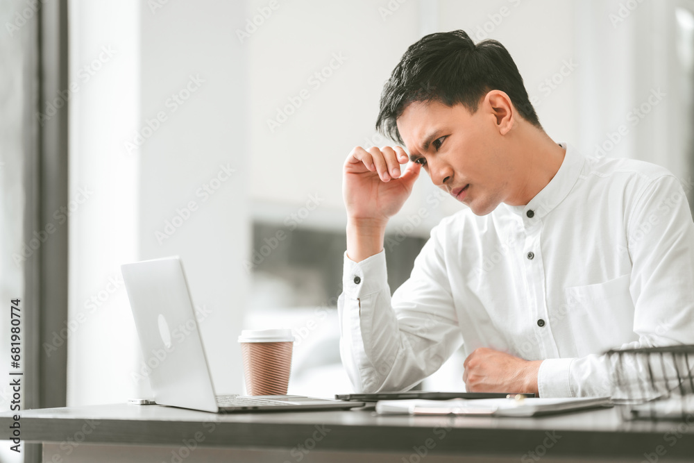 Asian male people concerned person in white shirt looks at laptop, possibly stressed, hand on their forehead. middle age businessman Asian male people concerned person in white shirt looks at laptop, possibly stressed, hand on their forehead. middle age businessman