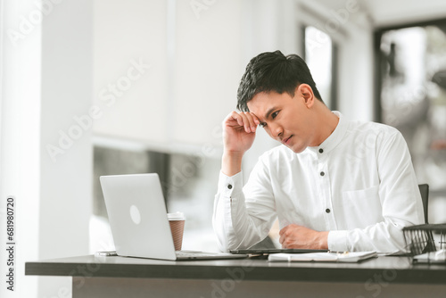 Asian male people concerned person in white shirt looks at laptop, possibly stressed, hand on their forehead. middle age businessman