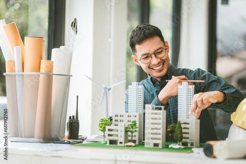 Asian people joyful person businessman engineer holding building model with wind turbines, representing clean energy city with low air pollution, surrounded by more models.