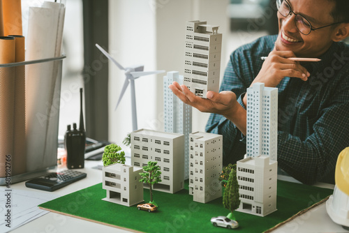 Asian people joyful person businessman engineer holding building model with wind turbines, representing clean energy city with low air pollution, surrounded by more models.