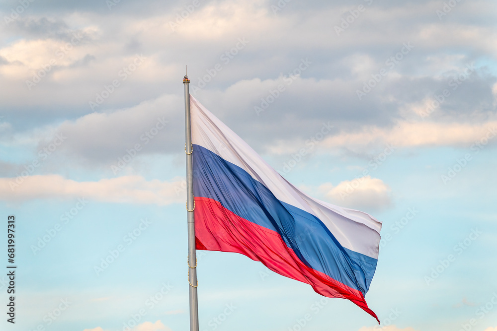 Russian tricolor flag waving in the wind against a blue sky.