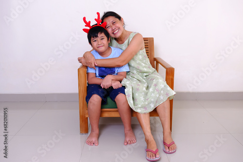 Asian mother with his chubby little boy wearing reindeer horn hair band in his head, sitting on the sofa celebrating Christmas photo