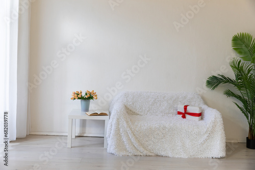 Interior of a white room with a sofa, a window and flowers