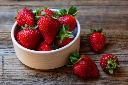 Fresh red strawberries, organic strawberries in white bowl on wooden background, close-up.