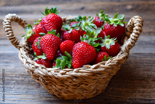Fresh red strawberries, organic strawberries in wicker basket on wooden background, close-up.
