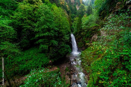 A long waterfall flowing through green trees in the forest when the weather is slightly cold in autumn. Natural wonder waterfall. Distance view of the waterfall.