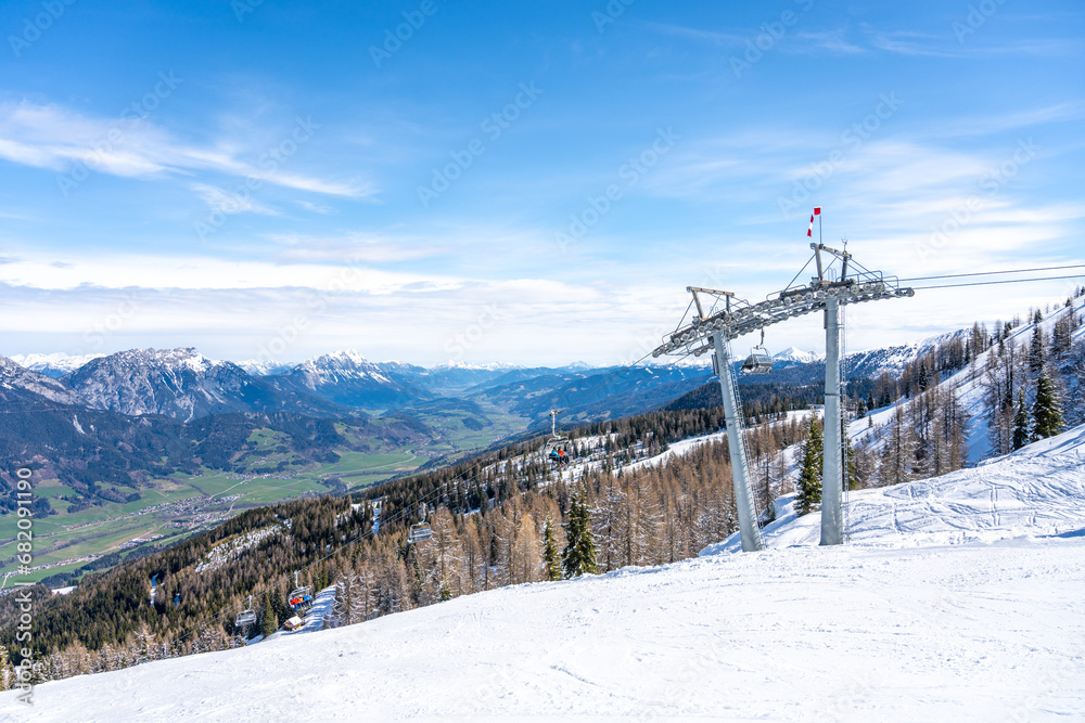 Ski lift in alpine ski resort. Late winter snow in the mountains and green grass in the valley. Schladming, Austria