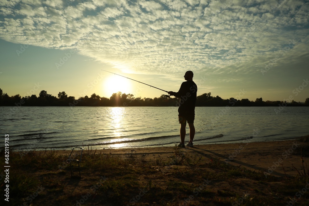 Fisherman with rod fishing at riverside at sunset