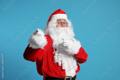 Merry Christmas. Santa Claus pointing at something on light blue background