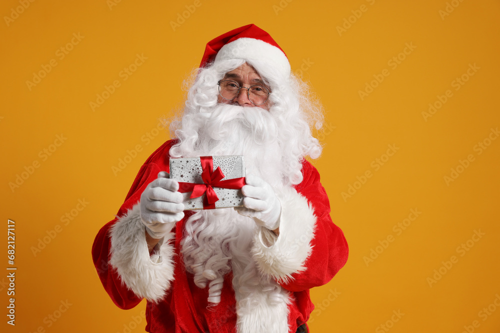 Santa Claus holding Christmas gift on orange background Santa Claus holding Christmas gift on orange background