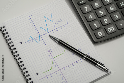 Wykresy narysowane w zeszycie od matematyki, obok leży kalkulator