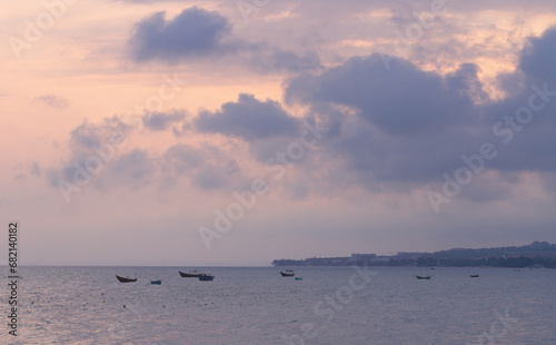 Sunset over the sea in Vietnam. Seascape in beautiful pink and purple tones. Small fishing boats against the background of the coastline