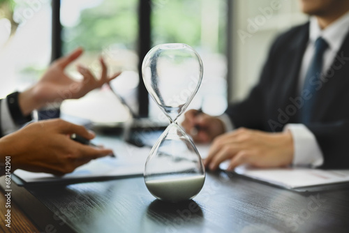 Closeup hourglass on meeting table with blurred two businesspeople working on background photo