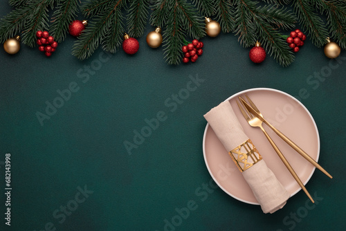 Christmas table top view: empty plate, golden cutlery. Festive setting, New Year decorations. Shiny baubles, fir branches, evergreen tree. Celebration banquet. Dark green frame, gold and red ornaments