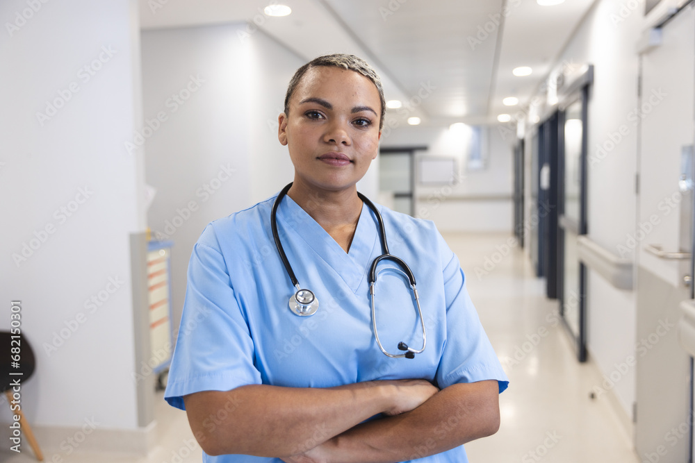 Portrait of happy biracial female doctor wearing scrubs and stethoscope in corridor at hospital