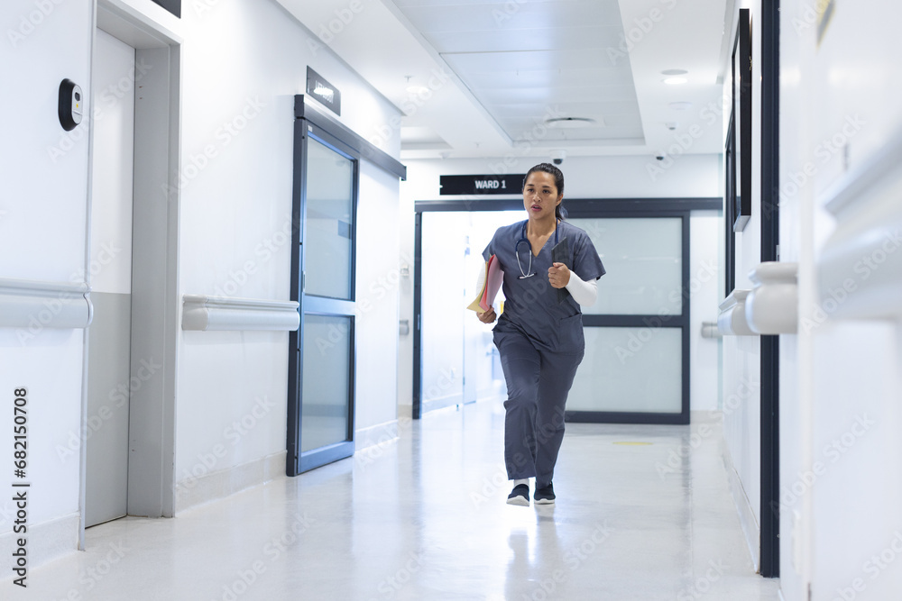 Biracial female doctor wearing scrubs running through corridor in hospital, copy space Biracial female doctor wearing scrubs running through corridor in hospital, copy space
