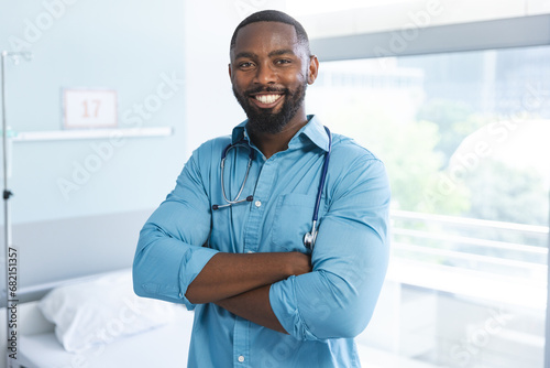 Portrait of happy african american male doctor wearing blue shirt and stethoscope in hospital room photo