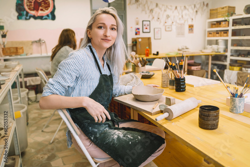 Female craftsperson working on ceramics tableware on pottery workshop.