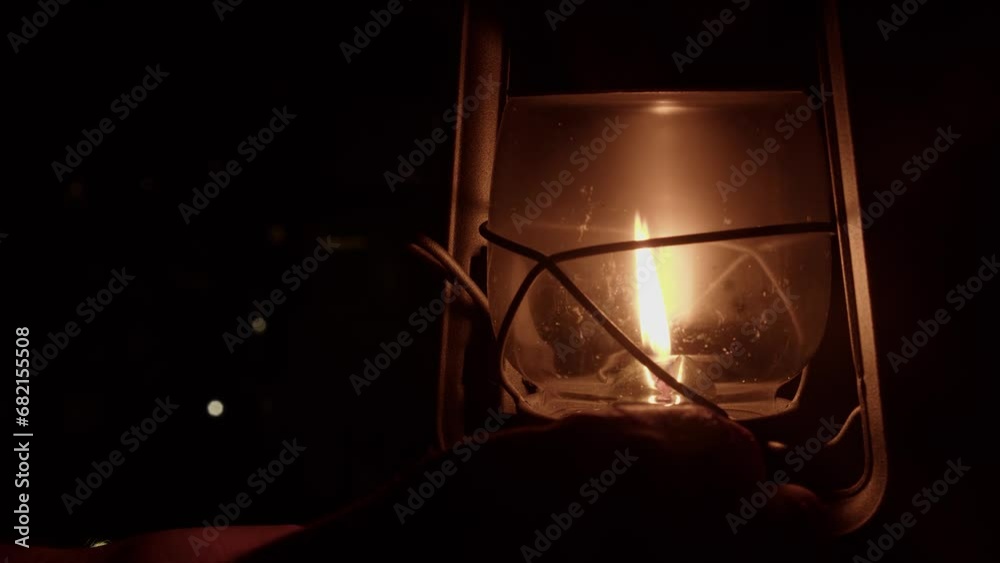 Dim night scene: Hand adjusts flame smaller in kerosene oil lantern