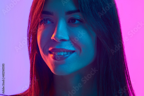 Close-up portrait of young beautiful brunette woman posing with smile against gradient pink studio background in neon light. Concept of human emotions  lifestyle  youth culture  facial expression