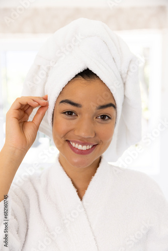 Portrait of happy biracial woman in bathrobe and with towel on her head in sunny bathroom