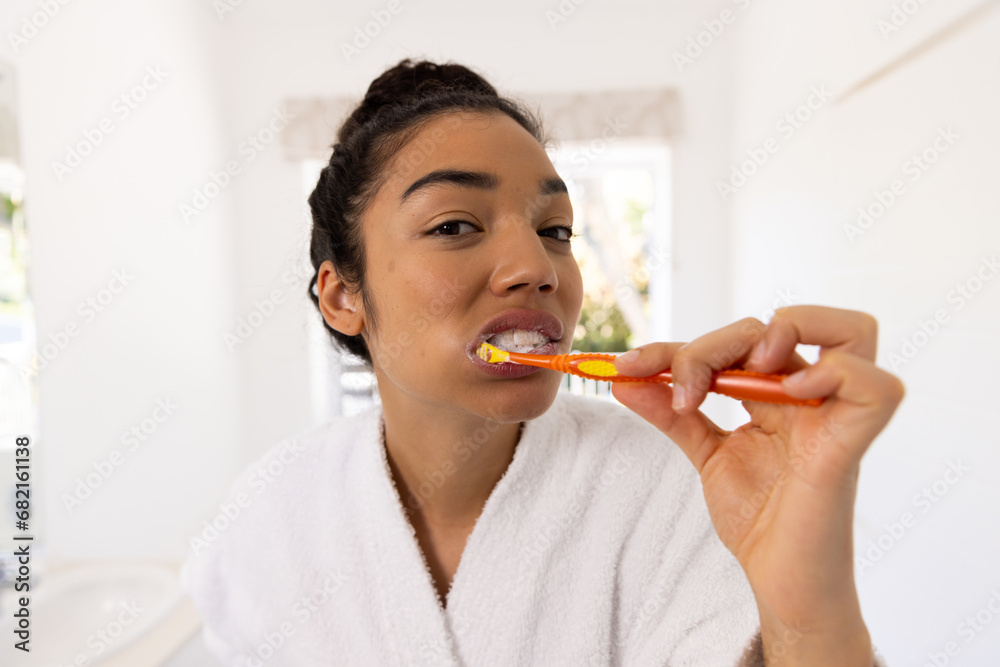 Portrait of biracial woman in bathrobe brushing teeth in sunny bathroom Portrait of biracial woman in bathrobe brushing teeth in sunny bathroom