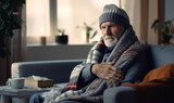 An elderly man in a hat and blanket looks tired and is freezing on the sofa in the apartment. The concept of heating and the cost of housing and communal services.