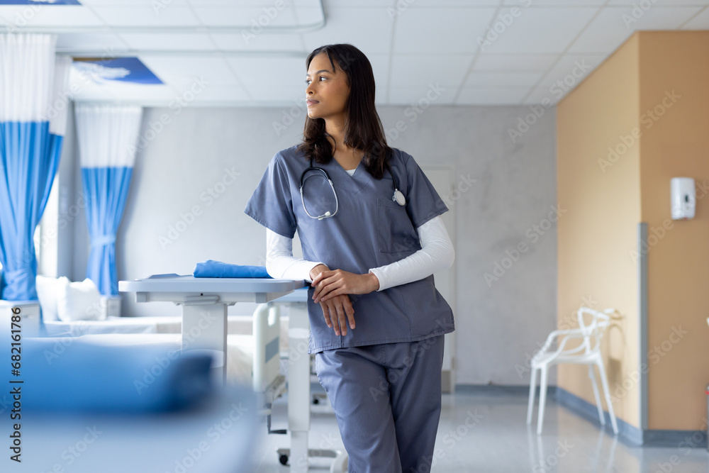 Biracial female doctor looking out window in sunny hospital room Biracial female doctor looking out window in sunny hospital room