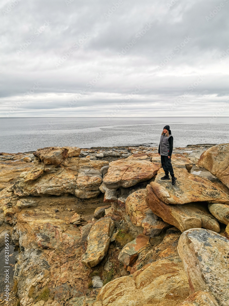 A girl on the shore of red stones next to the rocks of Two brothers on the Fishing Peninsula. The picturesque shore of the harsh Barents Sea. The North of Russia. The Kola Peninsula. The Arctic
