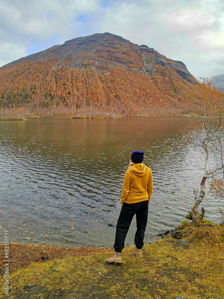 Golden autumn in the Arctic mountains beyond the Arctic Circle. A woman on the background of a beautiful lake and yellow birches. Autumn in the Khibiny Mountains.