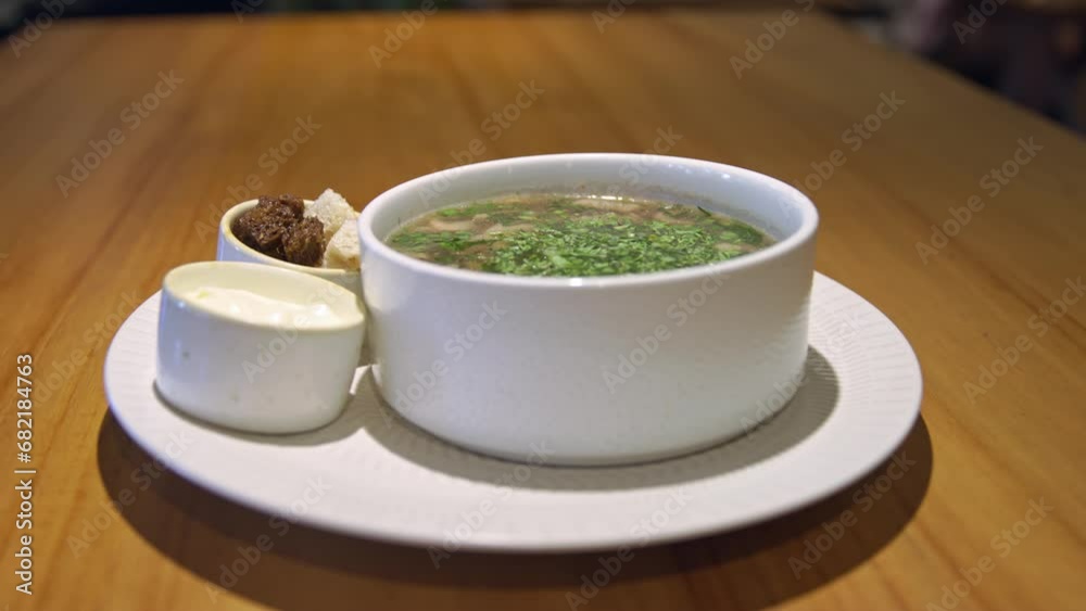 A bowl of soup with croutons and sour cream, sprinkled with herbs. Hot freshly brewed soup in a white plate is on the table, fried croutons, sour cream or mayonnaise, soup for lunch.