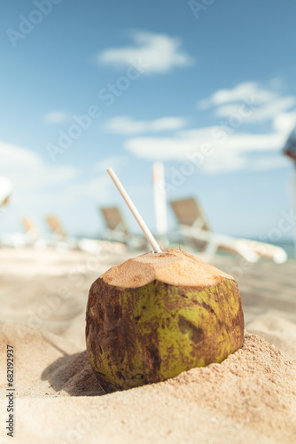 green Coconut in the sand with a straw in it