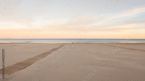Big sea beach at sunset and the horizon. Empty sea beach with yellow sand. Pink sunset over the sea. The coast in the evening at the resort. Alicante, Costa Blanca, Spain