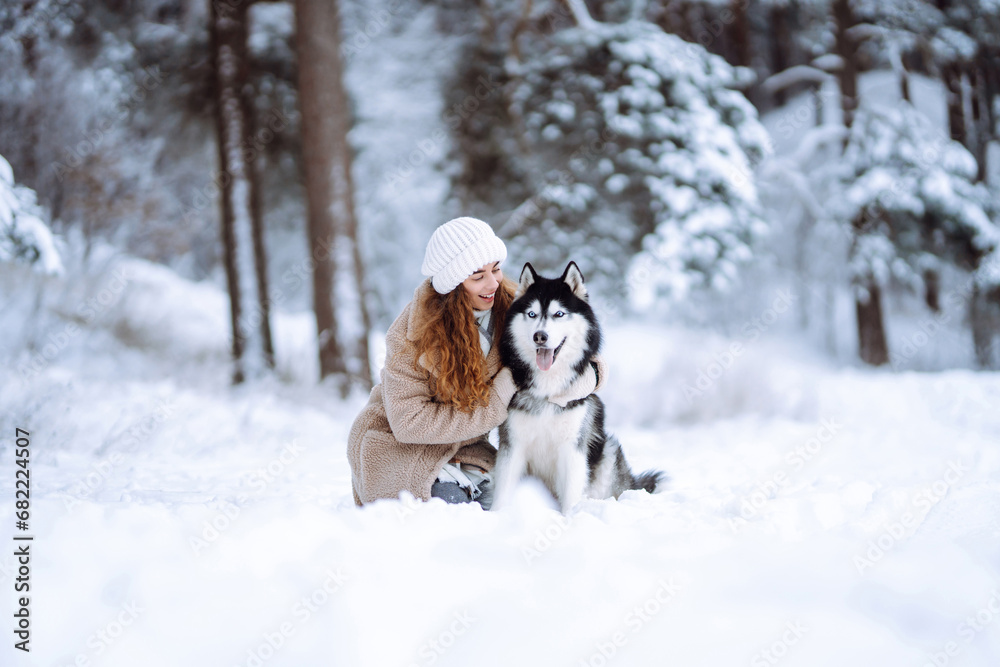 Beautiful young woman walks through the winter forest with her dog. A young woman with her pet on an adventure. Friendship concept, pets. Friendship between a woman and a dog. 