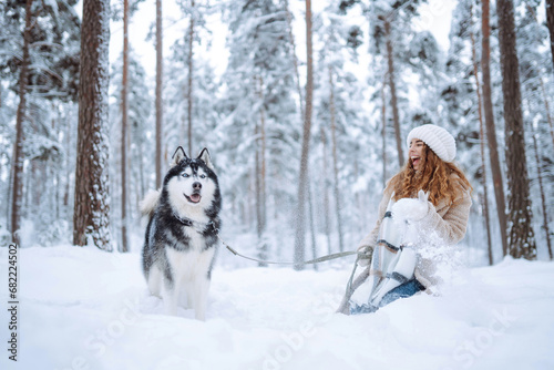 Beautiful young woman walks through the winter forest with her dog. A young woman with her pet on an adventure. Friendship concept, pets. Friendship between a woman and a dog. 