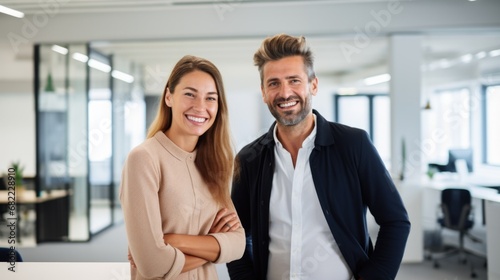 Portrait of smiling mature Hispanic Latin business man and European business woman standing arms crossed in office. Two diverse colleagues, group team of confident professional business people.