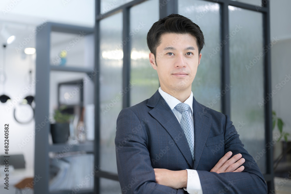 Smiling young businessman standing in his office, arms crossed, executive atmosphere. Smiling young businessman standing in his office, arms crossed, executive atmosphere.