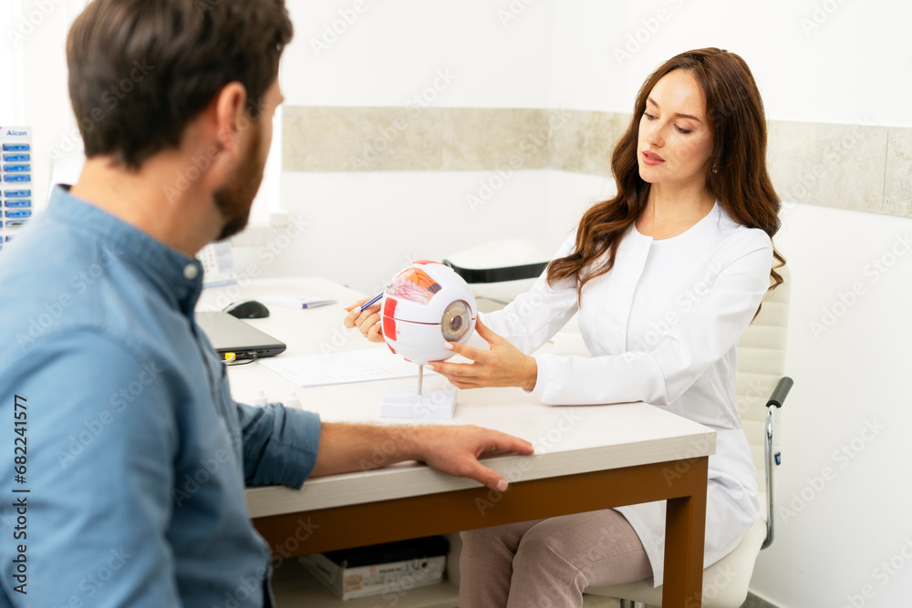 Female doctor holding eyeball model and talking with male patient Female doctor holding eyeball model and talking with male patient