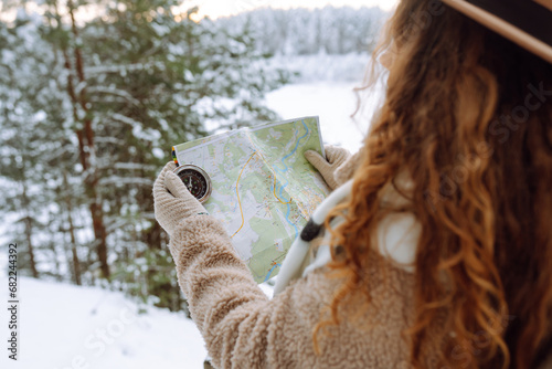 Beautiful woman traveler holds a compass and map in her hands. She is wearing a winter jacket, hat, scarf and backpack. Enjoying winter travel. Active lifestyle. Travel concept.