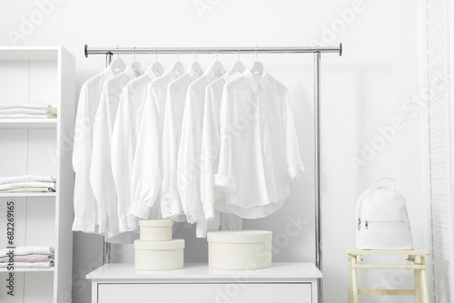 Wardrobe organization. Rack with different stylish clothes, shelving unit and folding ladder near white wall indoors © New Africa