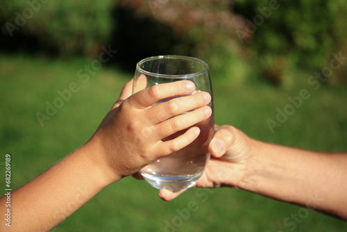 Child giving glass of water to elderly woman outdoors on sunny day, closeup